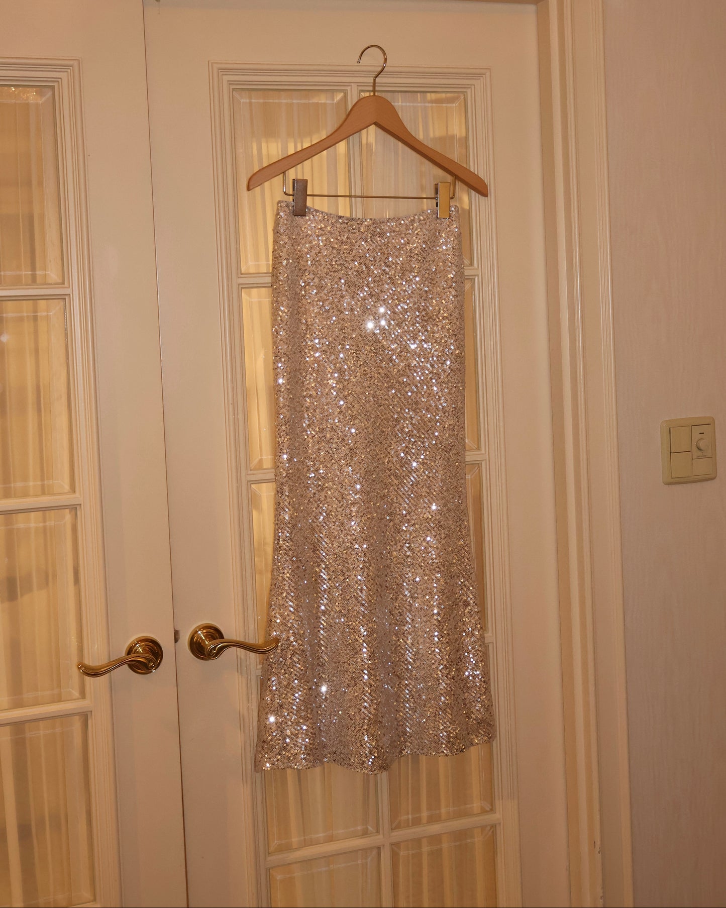 Champagne gold sequin mermaid skirt hanging on ivory wooden door.
