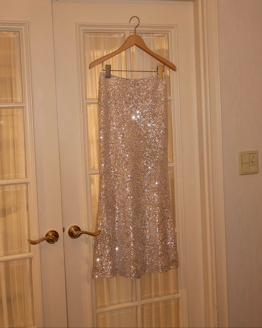 Champagne gold sequin mermaid skirt hanging on ivory wooden door.