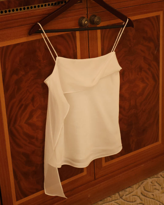 A white camisole top with thin straps hanging on a dark wooden hanger against a polished wood cabinet door.